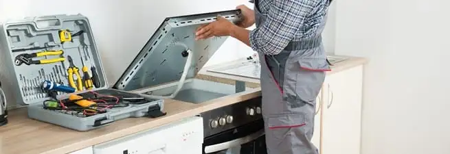 Cooktop repair technician lifting a built-in stovetop for service in Dayton, OH
