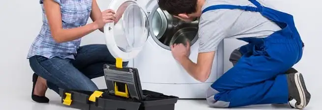 Washer repair technician inspecting a front-load washing machine with tools in Dayton, OH