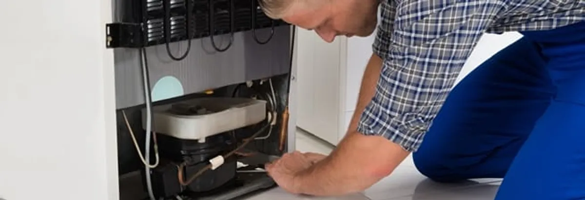 Refrigerator repair technician servicing the compressor and condenser area in Dayton, OH