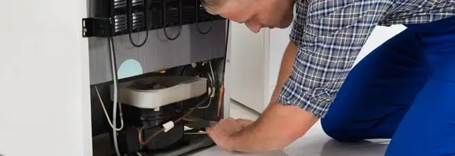 Refrigerator repair technician servicing the compressor and condenser area in Dayton, OH