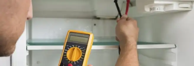 Refrigerator repair technician testing electrical components with a multimeter in Dayton, OH